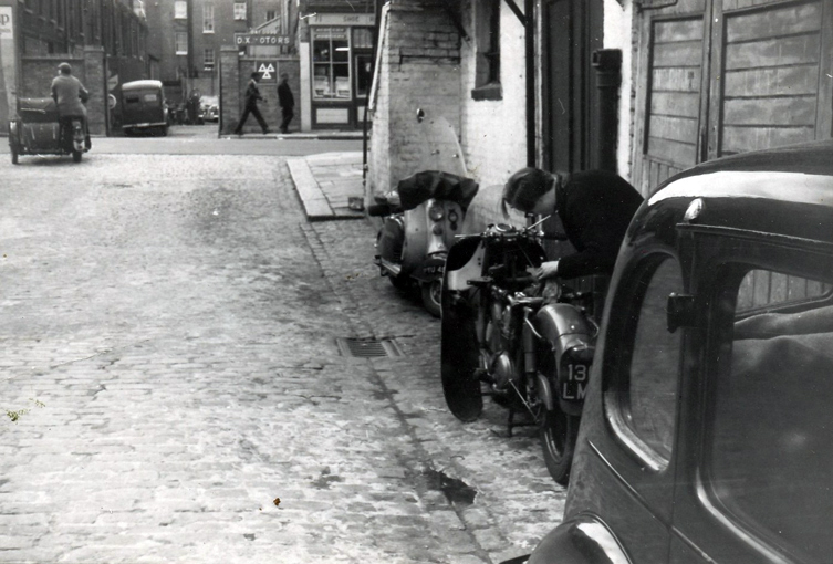 JM working on his motorbike, outside his flat on Chepstow Road, West London. Circa 1962